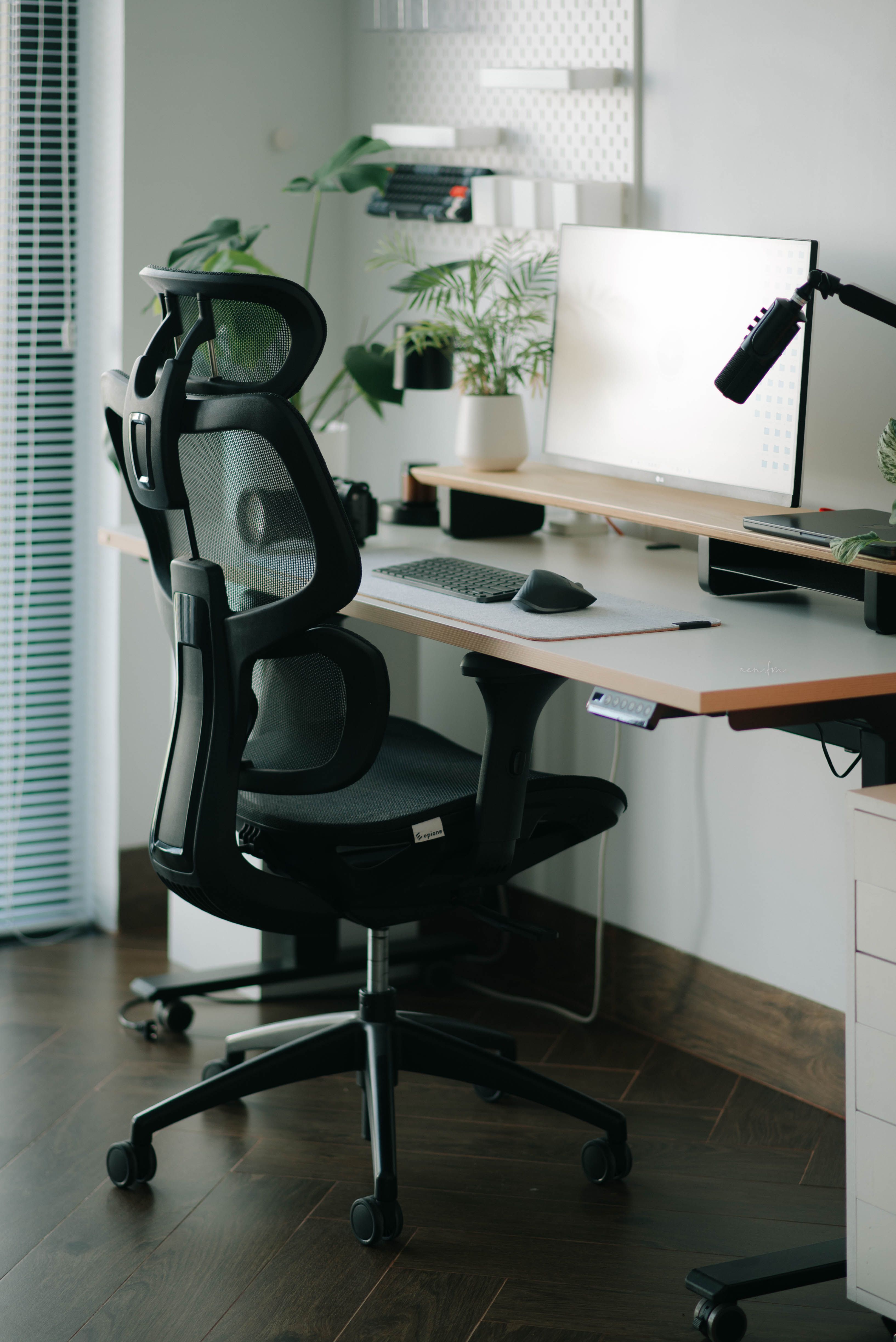 Ergonominen toimistotuoli, jossa käsinojat, korkeussäädettävän pöydän ääressä näyttöineen